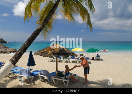 Eldery mari épouse donnant un verre sous un parapluie de paille sur la plage de Little Bay Saint Maarten île des Caraïbes Banque D'Images