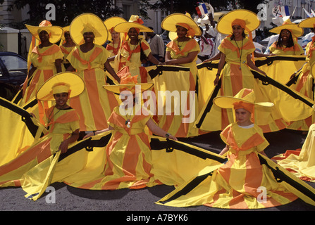 Groupe adulte jeunes femmes et jeunes vêtus de robes rayées orange jaune dans la scène de rue ensoleillée à Londres 1992 Notting Hill Carnival Parade UK Banque D'Images