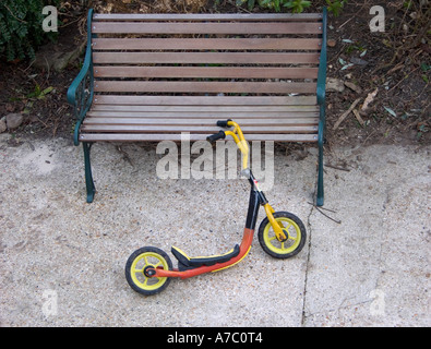 Scooter enfant appuyée sur le métal et le banc en bois, sur le chemin de béton Banque D'Images