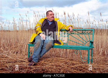 L'homme en faisant une pause sur un banc dans l'Irlande de champ de roseaux Banque D'Images