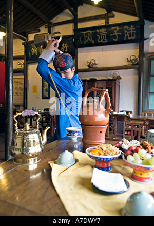 HANGZHOU, Chine thé thé jeune serveur verse de derrière son dos à l'aide d'un bec long teapot Banque D'Images