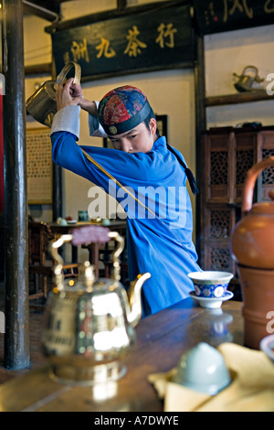 HANGZHOU, Chine thé thé jeune serveur verse de derrière son dos à l'aide d'un bec long teapot Banque D'Images