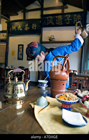 HANGZHOU, Chine thé thé jeune serveur verse de derrière son dos à l'aide d'un bec long teapot Banque D'Images