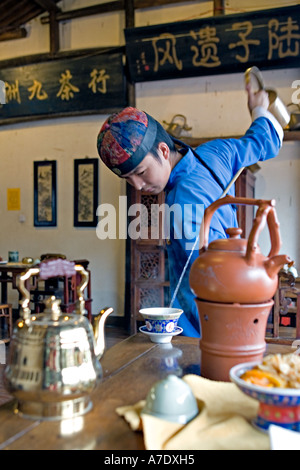 HANGZHOU, Chine thé thé jeune serveur verse de derrière son dos à l'aide d'un bec long teapot Banque D'Images