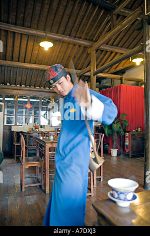 HANGZHOU, Chine thé thé jeune serveur verse de derrière son dos à l'aide d'un bec long teapot Banque D'Images