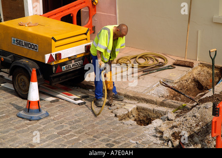 Travaux Workman utilise un marteau pneumatique pour creuser un trou dans la route de l'Angleterre Banque D'Images