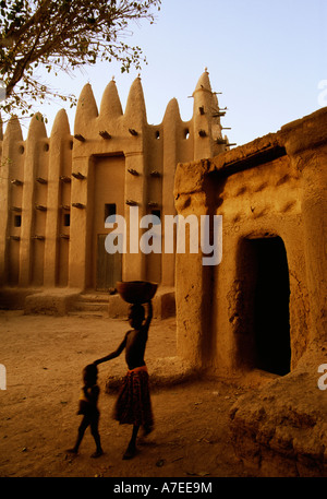 Senossa, nr Djenne, Mali ; une fille porte une calebasse sur la tête en face de la mosquée de style soudanais Banque D'Images