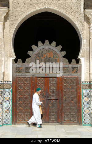 Homme portant un tissu traditionnel en face d'une vieille porte en bois sculpté, Medersa Bou Inania Fez El-Bali Maroc Banque D'Images