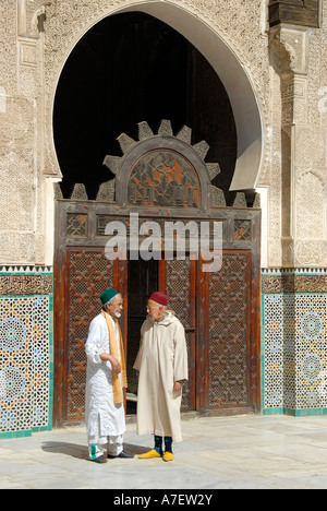 Les hommes portant des tissus traditionnels se tenir devant une vieille porte en bois richement sculptés de parler Medersa Bou Inania Fez El-Bali Maroc Banque D'Images