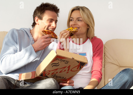 Couple sitting on sofa de manger une pizza à emporter en soirée confortable Banque D'Images