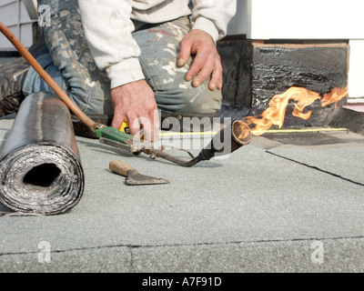 Couvreur sur les genoux d'installer un nouveau feutre bitume sur 'plat' toit du garage, rouleau de plomb et de gaz Flamme torche clignotante England UK Banque D'Images