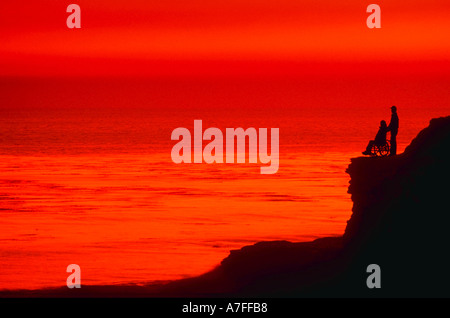 Silhouette de personne debout avec personne en fauteuil roulant contre le coucher du soleil Banque D'Images