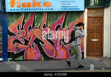 L'homme sur téléphone mobile en passant devant la boutique fermée avec volets vers le bas, Brighton, Angleterre, Royaume-Uni, 18 mars 2006. Banque D'Images