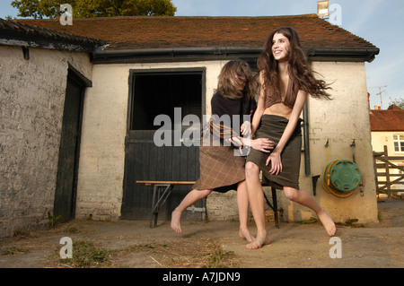 Deux jeunes filles en jupe les taquineries les uns les autres en face d'un stable dans une arrière-cour. Banque D'Images