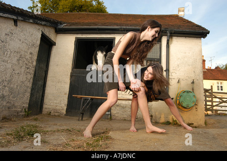 Deux jeunes filles en jupe les taquineries les uns les autres en face d'un stable dans une arrière-cour. Banque D'Images