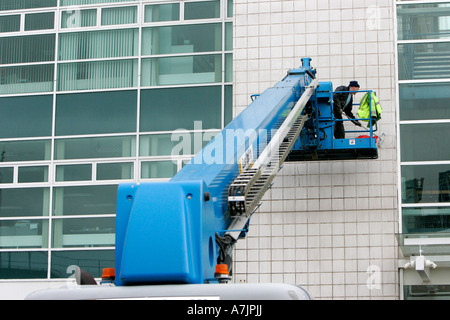 Vue arrière de l'ascenseur et des travailleurs sur la plate-forme Ascenseur ascenseur brushing mur extérieur d'un immeuble de bureaux avec du carrelage blanc belfast Banque D'Images