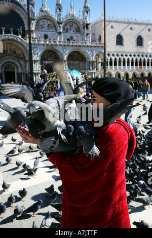 Vieille femme en robe rouge rss pigeons sur son bras en face de la cathédrale basilique Saint Marc Venise Italie central Europe EU Banque D'Images