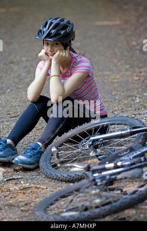 Fille assise sur le sol après avoir tomber de son vélo le long d'un chemin forestier Banque D'Images