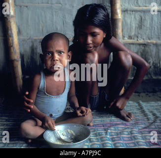 Jeune fille s'occupe de son petit frère et le nourrit de riz bol d'étain en cabane de torchis au Bangladesh Banque D'Images