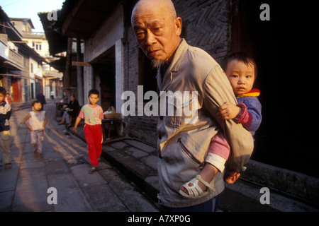 Chine, province du Sichuan, Shi Bao Zhai , ancien homme porte bébé à travers des rues du village le long du fleuve Yangtze Banque D'Images