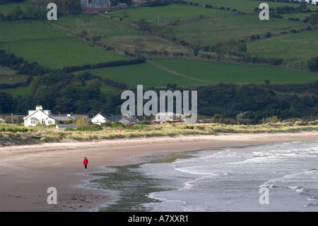 Femme au manteau rouge seul promenades le long de la plage de sable de glenarrif waterfoot le comté d'Antrim en Irlande du Nord Banque D'Images