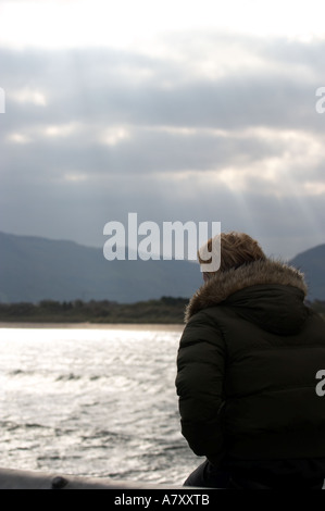 Woman se penche sur la mer et la baie rouge à partir de la jetée de waterfoot sur une journée froide comme la lumière du soleil perce les nuages glenariff Banque D'Images