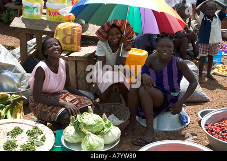 Marché alimentaire traditionnel en plein air en Afrique de l'Ouest avec des commerçants, avec 3 filles souriantes vendant des fruits et légumes dans la région occidentale du Ghana Banque D'Images