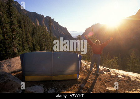 Un randonneur accueille le matin soleil qui se lève sur les montagnes à l'extérieur de sa tente avec les bras tendus, Banque D'Images