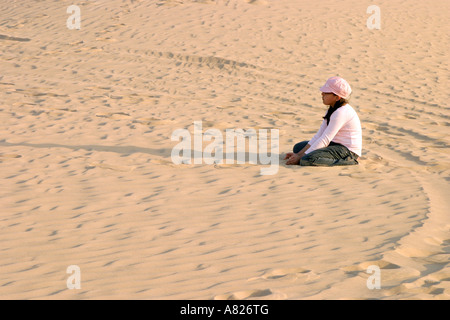 Une jeune fille dans un chapeau rose assis dans le désert d'Arabie, Abu Dhabi, UAE Banque D'Images