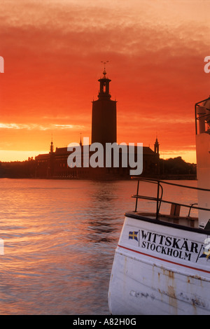 Bateau de pêche amarré à Riddharholmen à Stockholm avec l'Hôtel de Ville silhouetté contre le ciel au coucher du soleil Banque D'Images