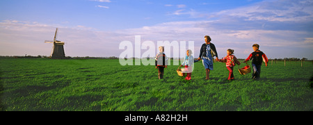 La mère et les enfants avec des paniers traversant les terres agricoles en Hollande près de Windmill Banque D'Images