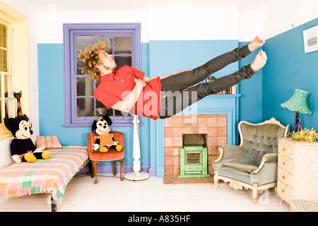 L'homme en robe serré tombant horizontalement dans une chambre peintes de couleurs vives avec des jouets en peluche. Banque D'Images
