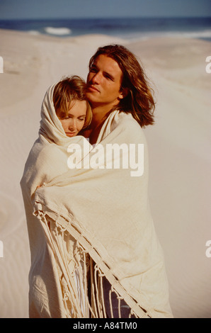 Couple enveloppé dans une couverture, debout sur une plage. Banque D'Images