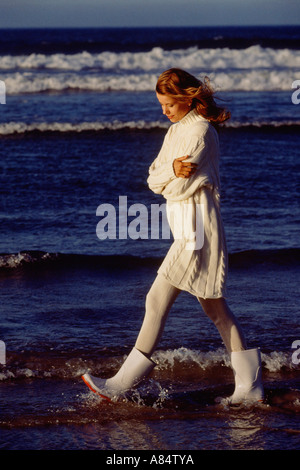 Femme portant une robe de laine blanche et bottes, marchant sur une plage. Banque D'Images