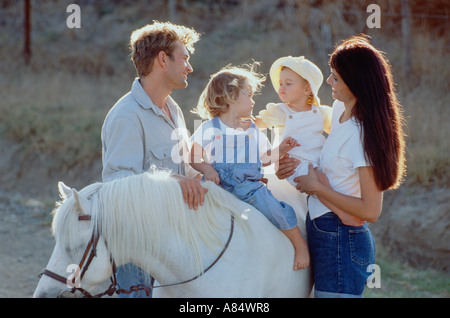 La famille. Les parents. Jeune couple avec deux enfants sur pony à l'extérieur. Banque D'Images