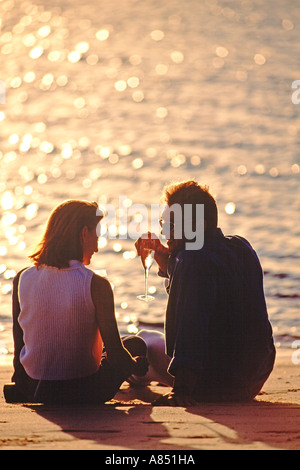 L'extérieur Vue arrière de young romantic couple homme et femme assis sur une plage au coucher du soleil. Banque D'Images