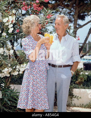 L'âge de la retraite couple en vacances, debout avec des verres de jus d'orange sur la terrasse extérieure. Banque D'Images