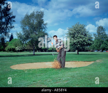 Le sport. Loisirs de l'établissement. Jeune homme jouant le golf. Ébrécher la balle d'un bunker de sable. Banque D'Images