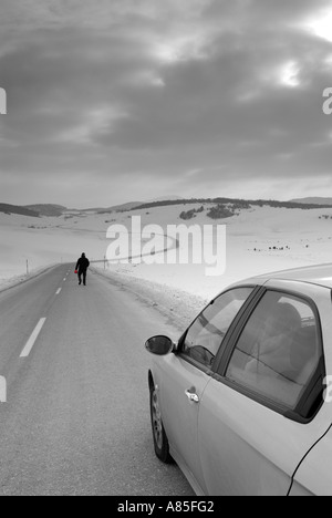 Homme quitte son conjoint dans la voiture pour marcher le long d'une route isolée dans la neige Banque D'Images