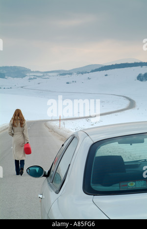 Femme commence la longue marche le long d'une route de campagne isolée en hiver pour trouver du carburant pour sa voiture en panne Banque D'Images