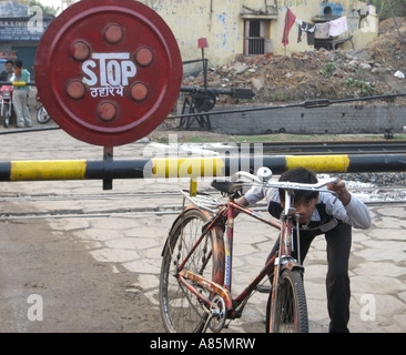 Un garçon en poussant son vélo sous une barrière sur un passage à niveau à Patna, Inde Banque D'Images