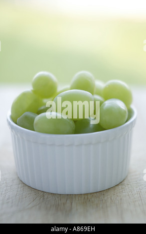 Groupe simple de raisins verts vide en ramakin dans un bol blanc placé sur une planche à découper de cuisine en bois utilisé Banque D'Images