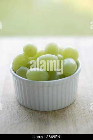 Groupe simple de raisins verts vide en ramakin dans un bol blanc placé sur une planche à découper de cuisine en bois utilisé Banque D'Images