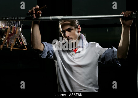 Young man leaning on un rack de vêtements tenant un cigare Banque D'Images