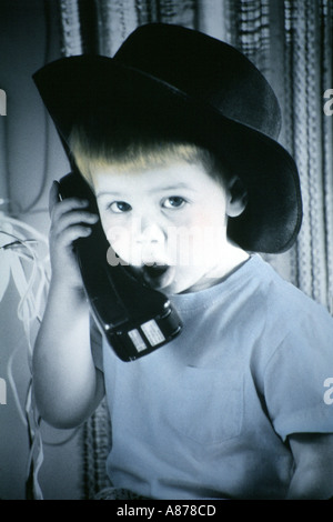 Un petit garçon portant un chapeau de cowboy à parler au téléphone. Photographie colorée à la main. Banque D'Images