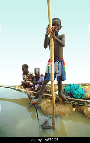 Jeunes enfants de la tribu Bozo assis dans un pirogue traditionnel et le jeune garçon pratiquant ses compétences pour punir. Dague Womina, Mali. Banque D'Images