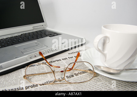 Open laptop portable avec les lunettes de journaux et une tasse de café sur une soucoupe tourné sur un fond blanc Banque D'Images