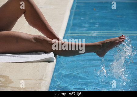Jambes de femme dans la piscine éclaboussant les pieds dans la piscine vacances détente Banque D'Images