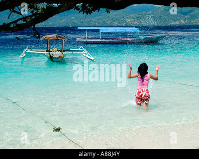 Femme mince,cheveux longs et noirs,en clair les éclaboussures/mer turquoise à côté de bateaux traditionnels, Gili Trawangan, Indonésie. Banque D'Images