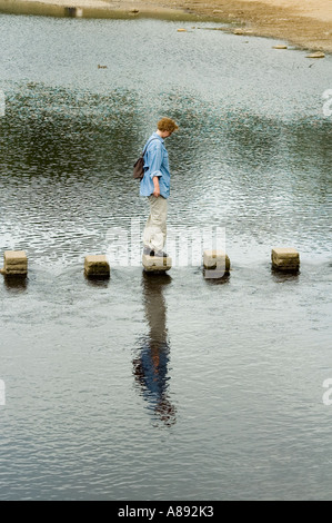 Woman balancing sur pierres de gué sur la rivière Wharfe à Bolton Abbey, Wharfedale, Yorkshire Dales National Park, England, UK Banque D'Images